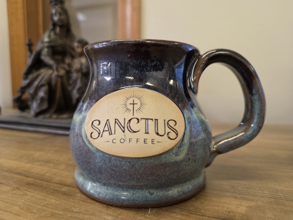 Sanctus Coffee Handmade Stoneware Potbelly Mug in Night Sky glaze with clay logo medallion before Madonna and Child statue
