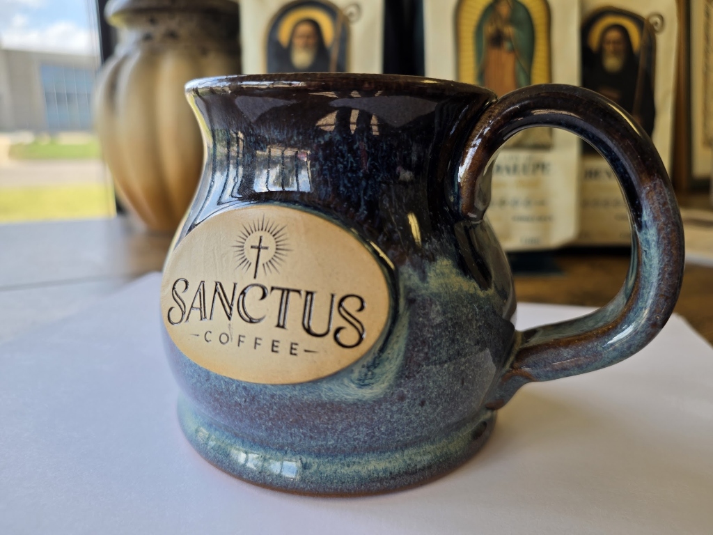 Sanctus Coffee Stoneware Mug on windowsill paired with St. Benedict, St. Joseph, and Our Lady of Guadalupe coffee bags